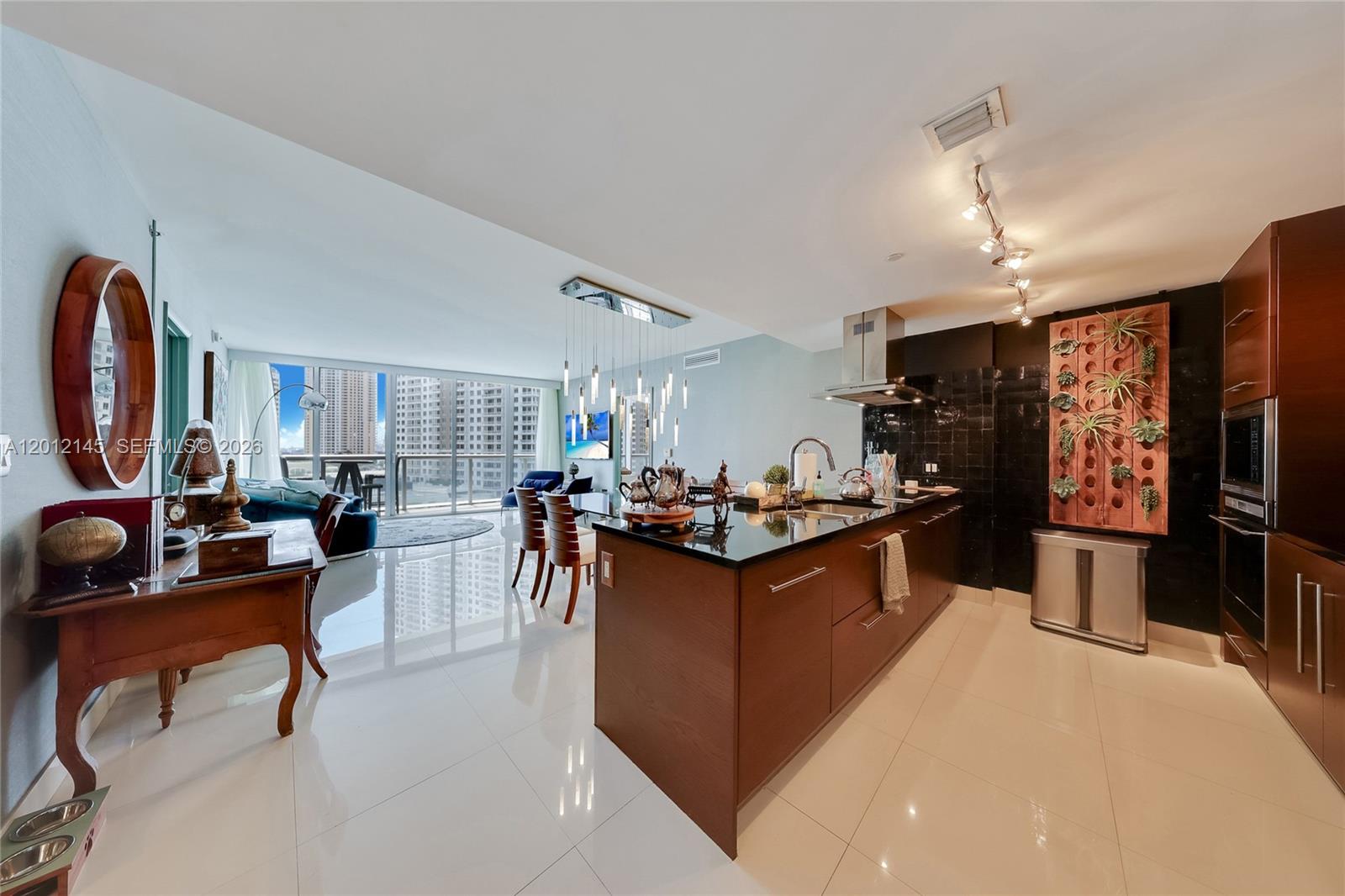 A modern kitchen with dark wood cabinetry and a black island overlooks a bright living area — 465 Brickell Ave # 1019, Miami FL 33131, MIAMI, FL