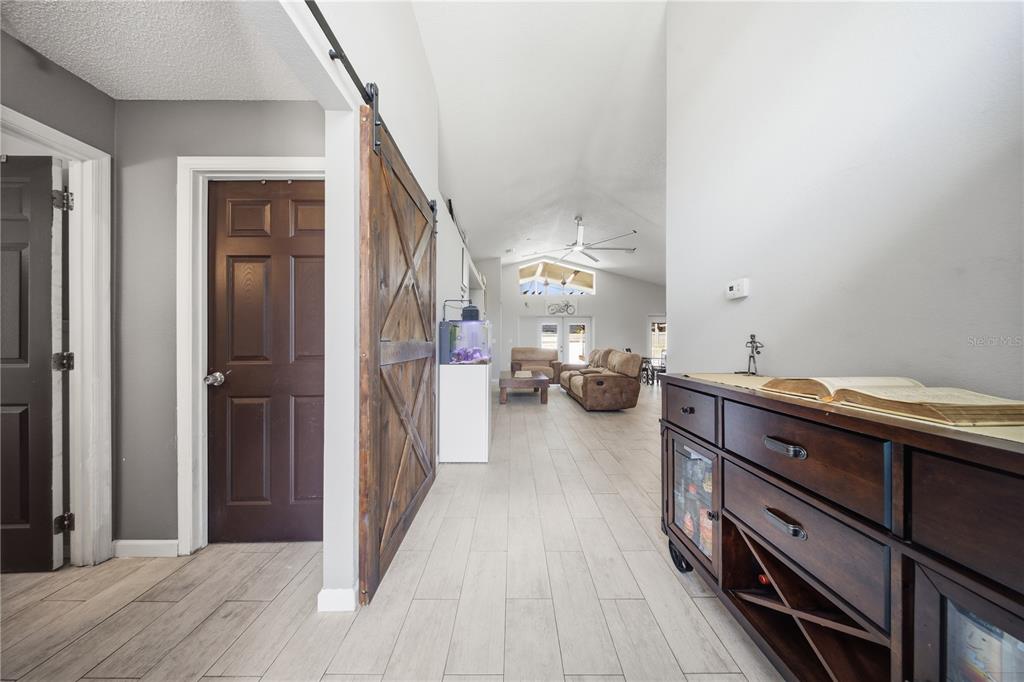 A hallway with light wood-look tile floors leads to a living room with vaulted ceilings — 4321 BAYSIDE DRIVE, KISSIMMEE, FL