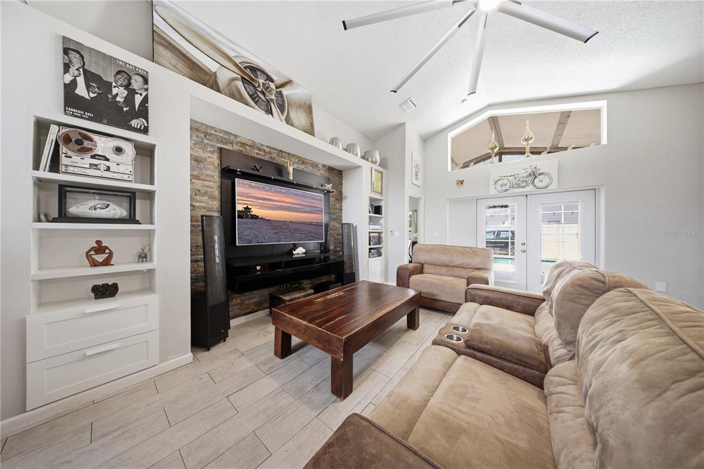 A living room features a stone accent wall with a mounted television and wood flooring — 4321 BAYSIDE DRIVE, KISSIMMEE, FL
