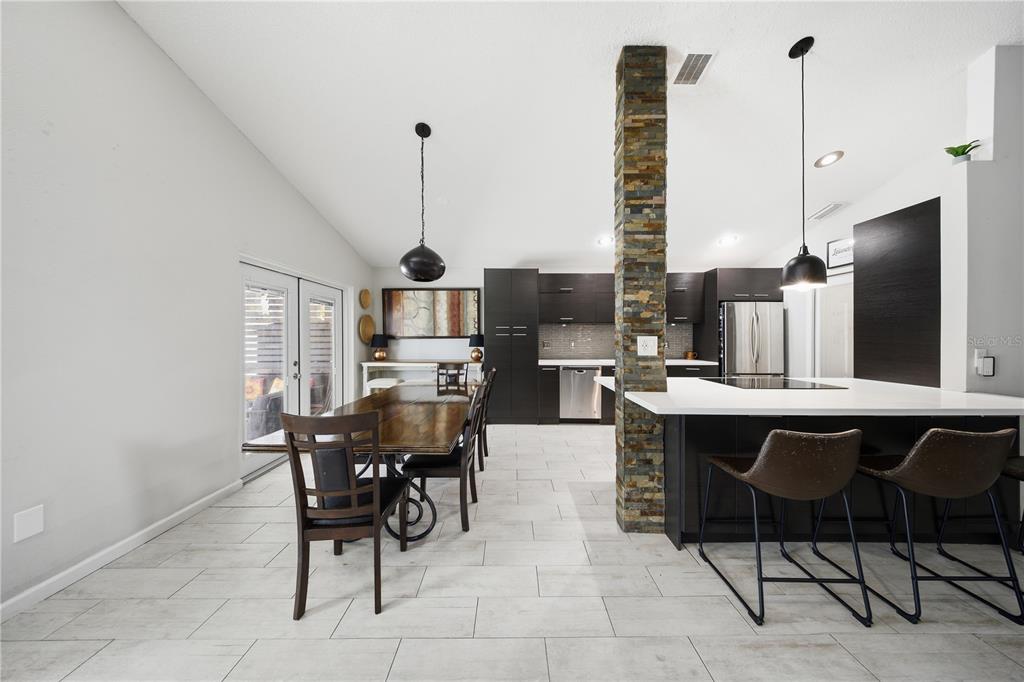 A modern kitchen and dining area features dark cabinetry, a stone pillar, and tile flooring — 4321 BAYSIDE DRIVE, KISSIMMEE, FL