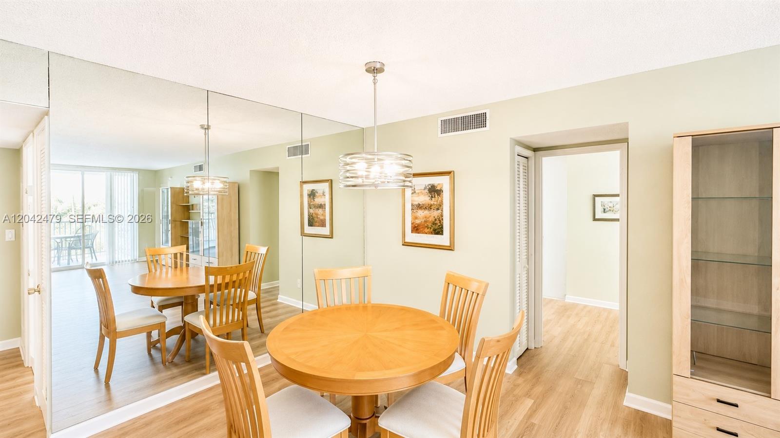 A dining room features a round wooden table, chairs, mirrored walls, and light wood flooring — 2671 S Course Dr # 208, Pompano Beach FL 33069, POMPANO BEACH, FL