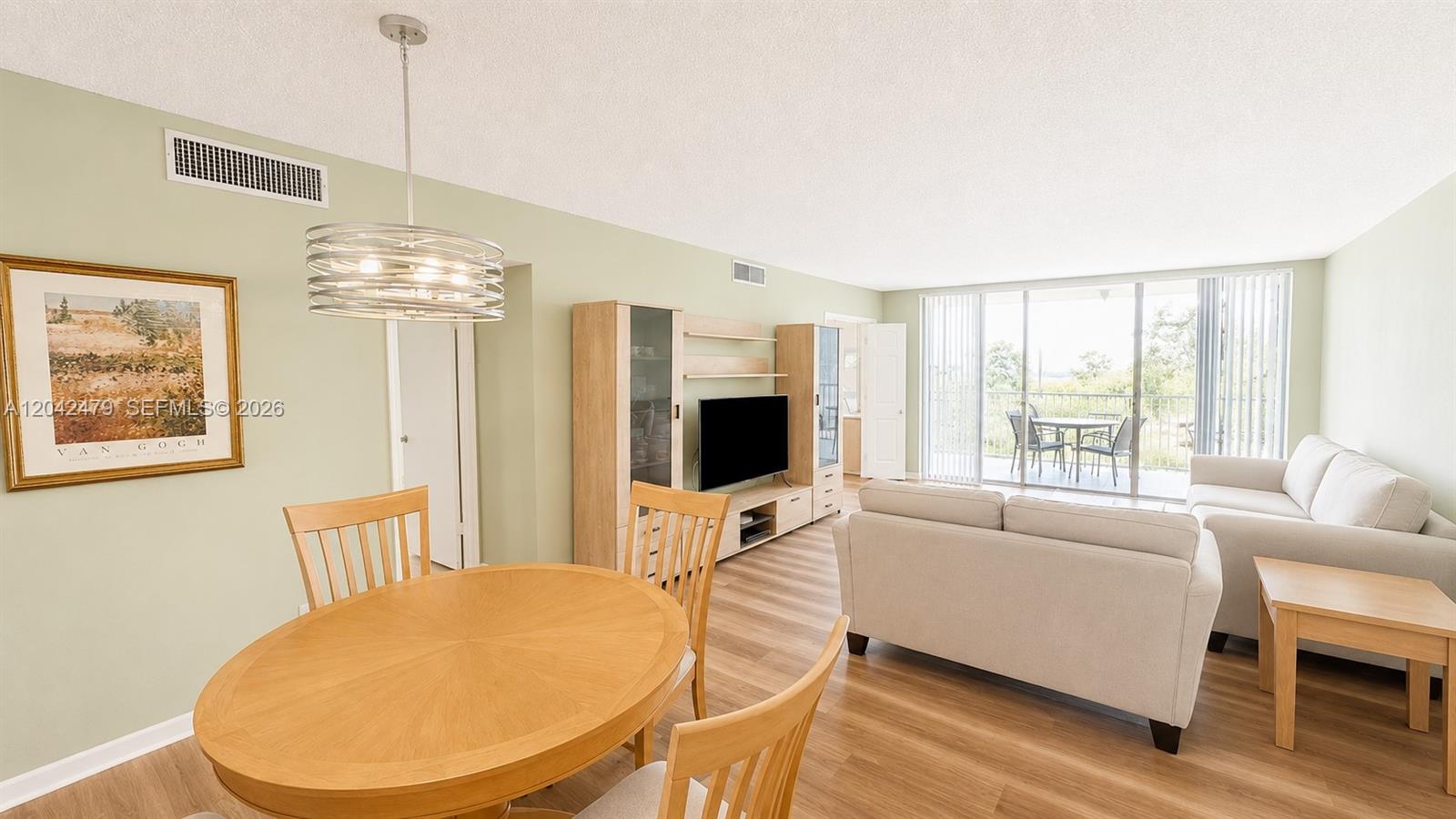 A living and dining area features light wood flooring, neutral furniture, and a balcony view — 2671 S Course Dr # 208, Pompano Beach FL 33069, POMPANO BEACH, FL