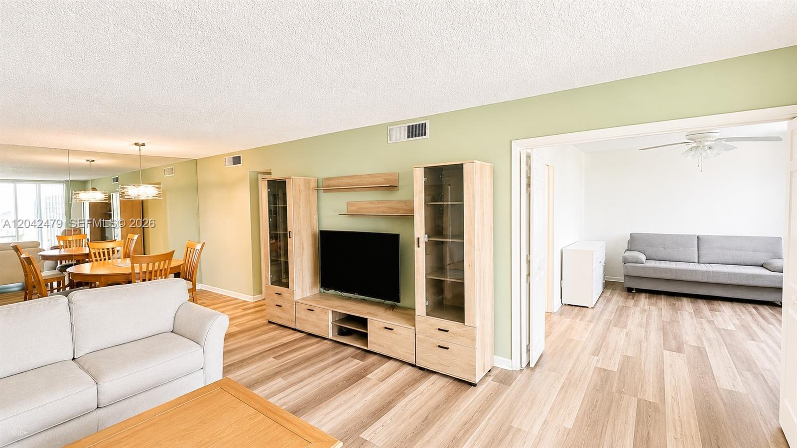 A living room features light wood flooring, a media console, and an adjacent dining area — 2671 S Course Dr # 208, Pompano Beach FL 33069, POMPANO BEACH, FL
