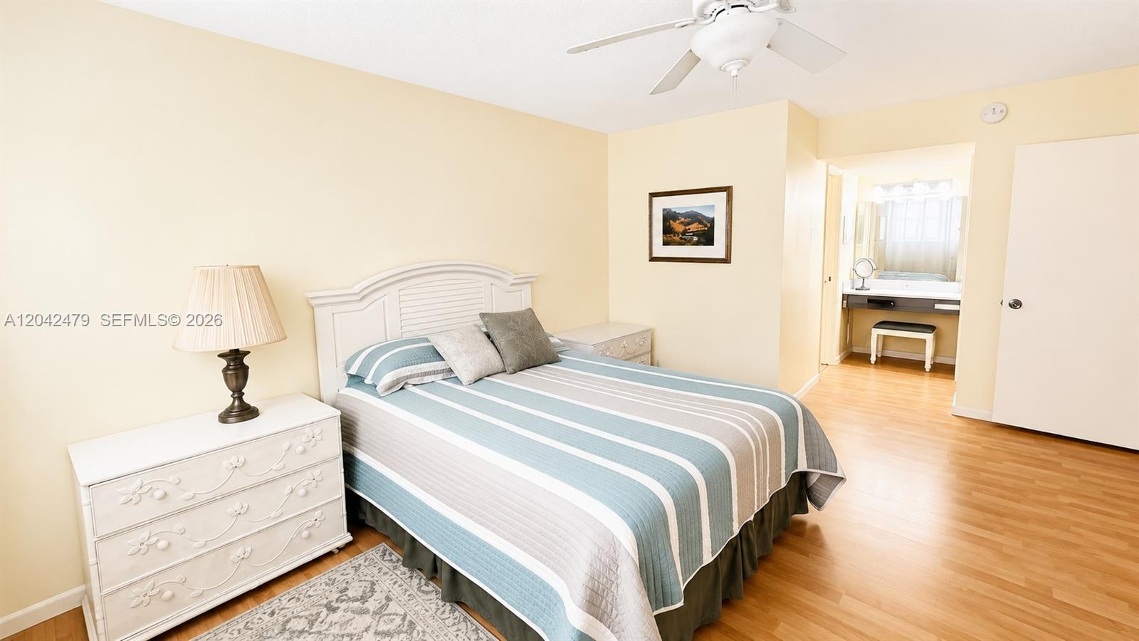A bedroom features a white bed frame, striped bedding, a ceiling fan, and wood flooring — 2671 S Course Dr # 208, Pompano Beach FL 33069, POMPANO BEACH, FL