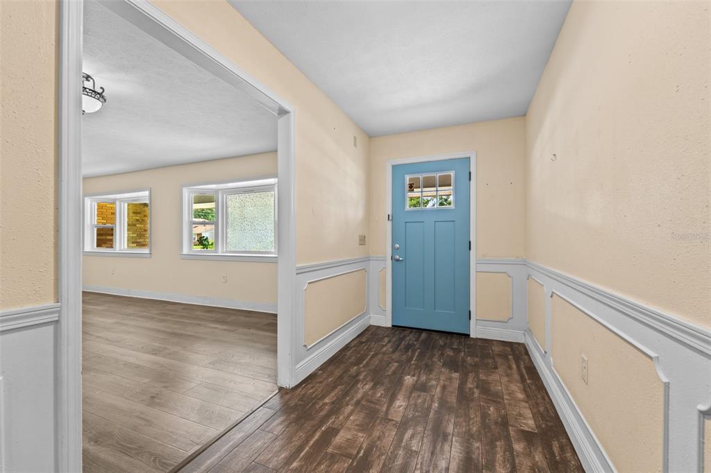 An entryway with a blue front door, wood-look flooring, and white wainscoting leads into a living room — 710 DEBRA LYNNE DRIVE, BRANDON, FL