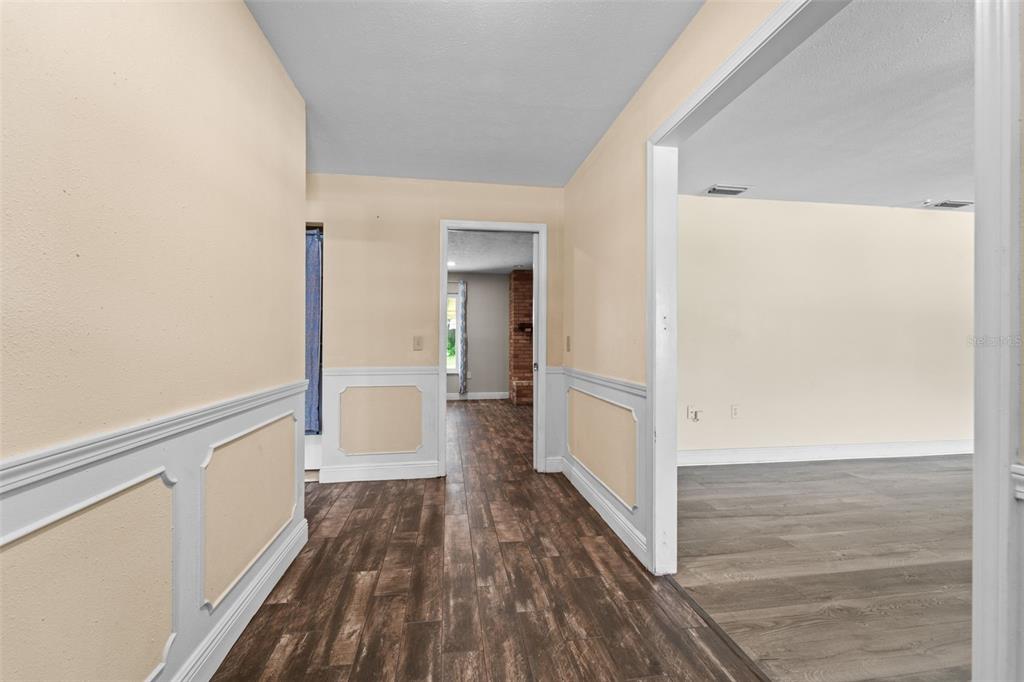 A hallway with wood-look flooring and wainscoting leads to a room with a brick fireplace — 710 DEBRA LYNNE DRIVE, BRANDON, FL