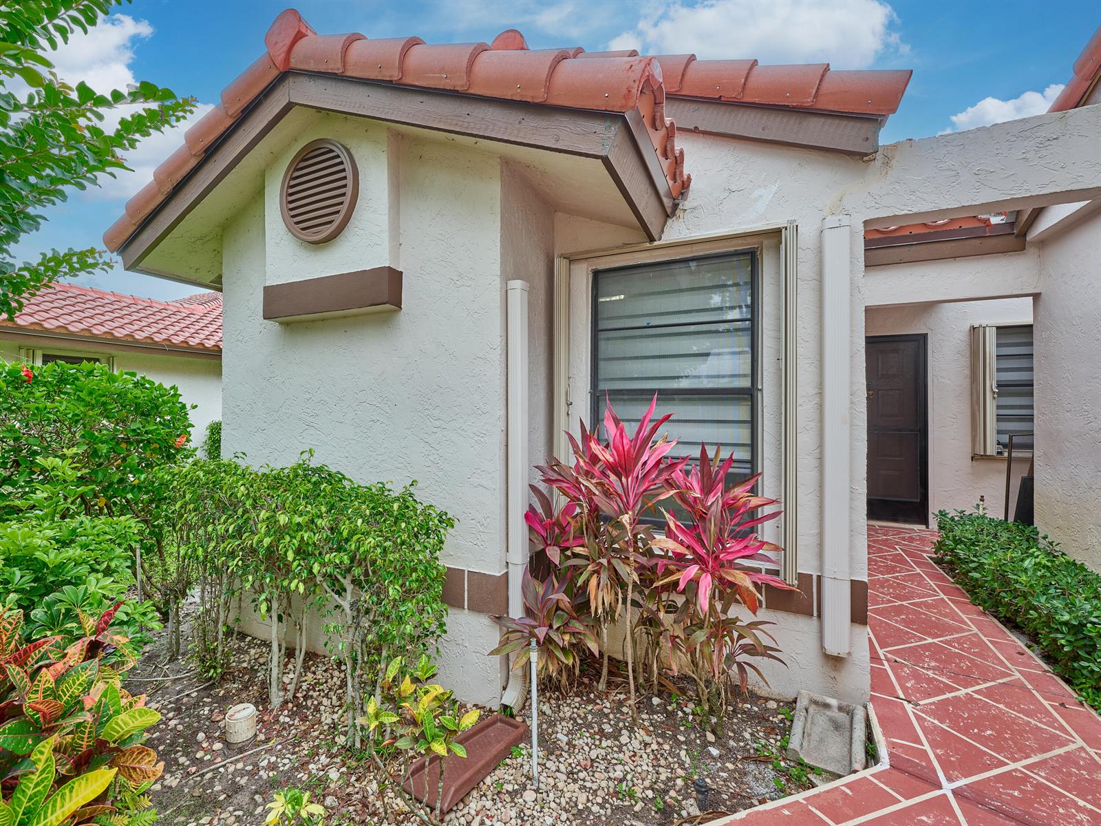 A stucco house exterior features a red tile roof, a window, and tropical landscaping — 6067 Kings Gate Circle, Delray Beach FL 33484, DELRAY BEACH, FL