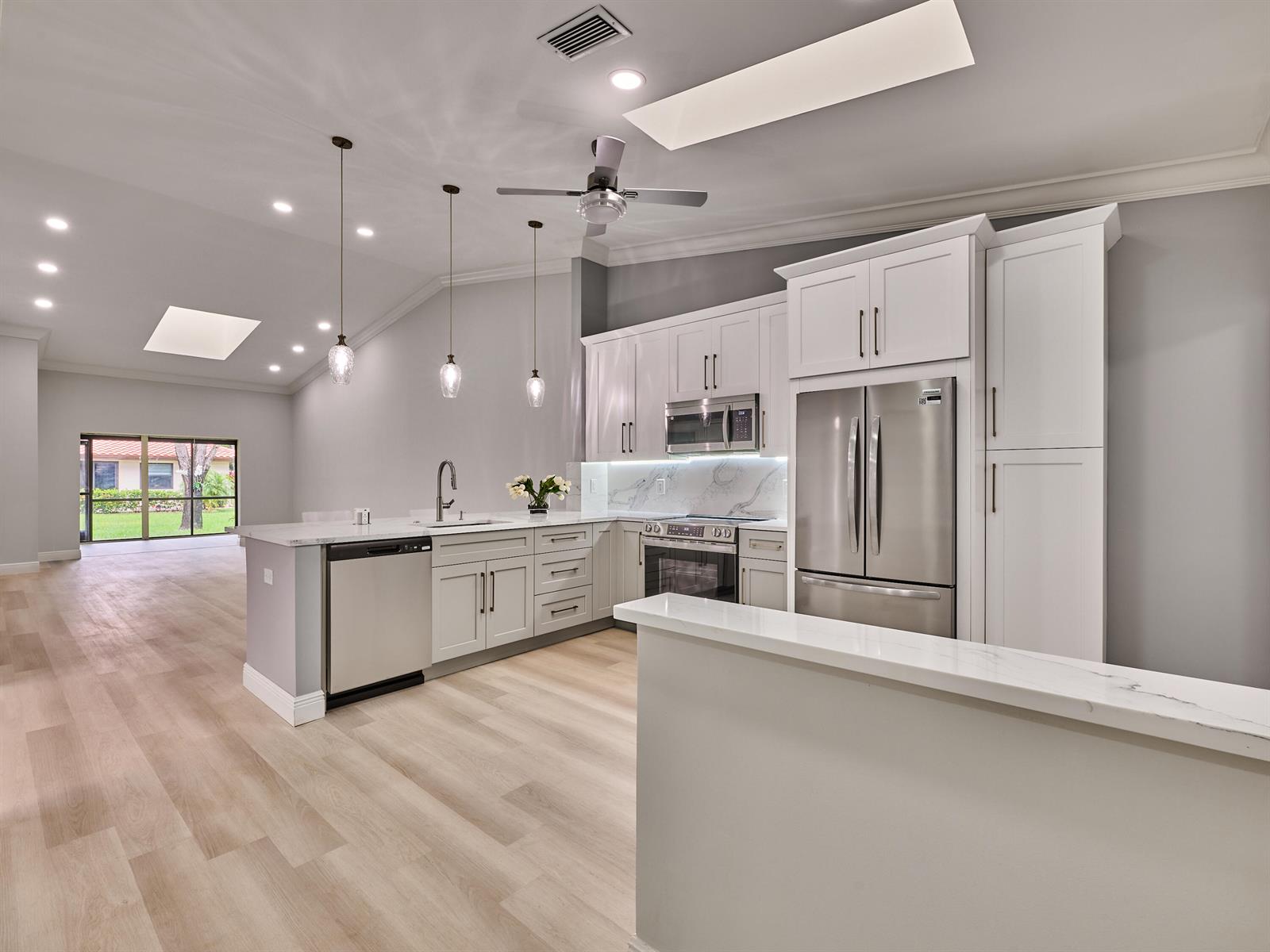 A modern kitchen features white cabinetry, stainless steel appliances, and light wood flooring — 6067 Kings Gate Circle, Delray Beach FL 33484, DELRAY BEACH, FL