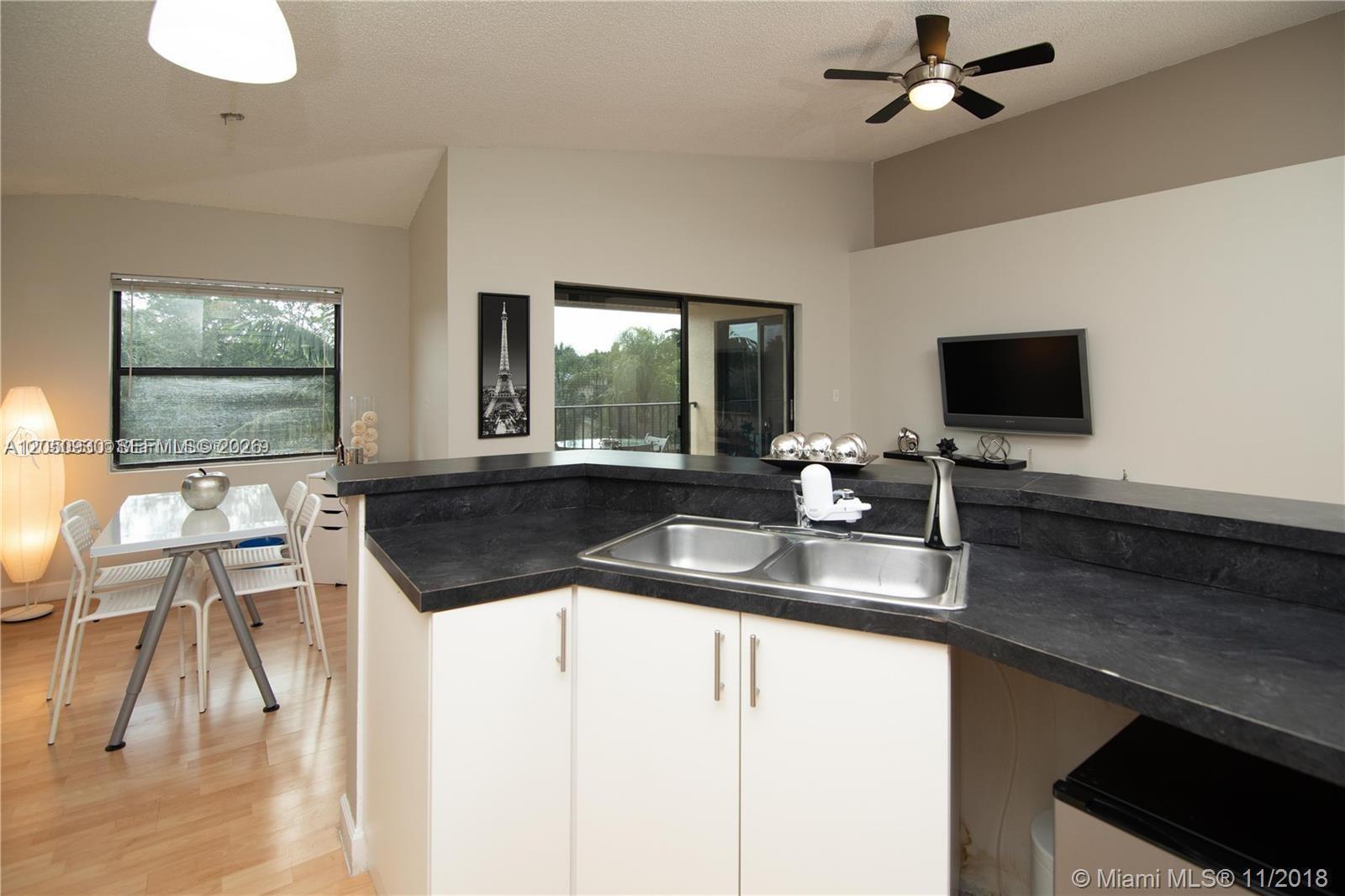 A kitchen with a dark countertop and double sink overlooks a dining area and balcony — 9999 Summerbreeze Dr # 403, Sunrise FL 33322, SUNRISE, FL