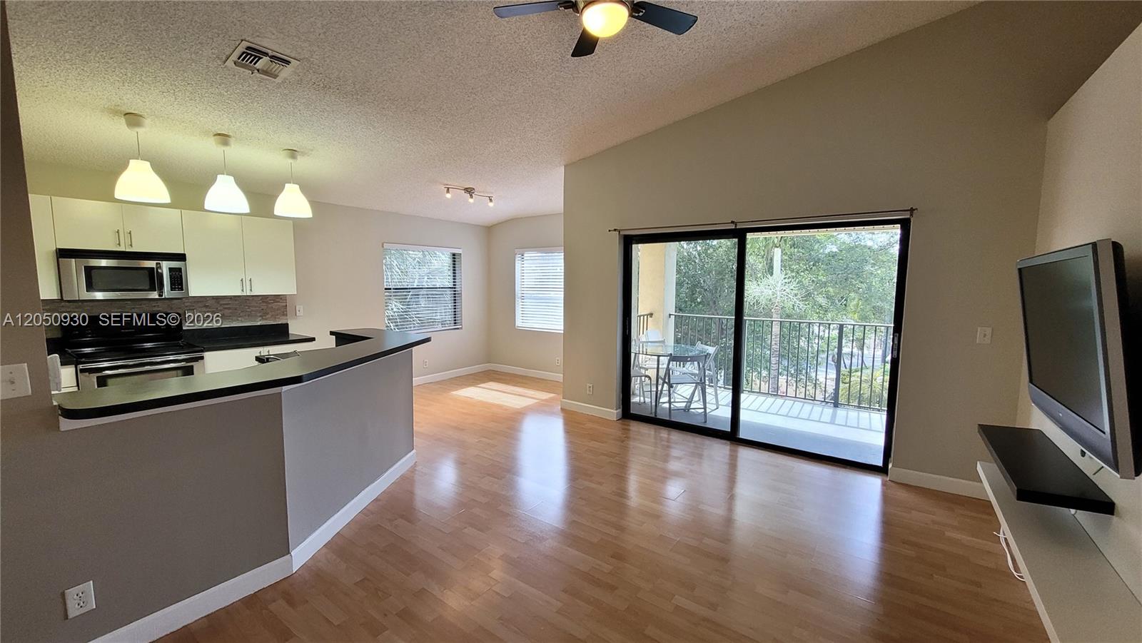 This open-concept living area features wood flooring, a kitchen breakfast bar, and a balcony — 9999 Summerbreeze Dr # 403, Sunrise FL 33322, SUNRISE, FL