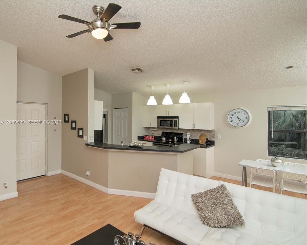 An open-concept living room and kitchen featuring light wood flooring and a white sofa — 9999 Summerbreeze Dr # 403, Sunrise FL 33322, SUNRISE, FL