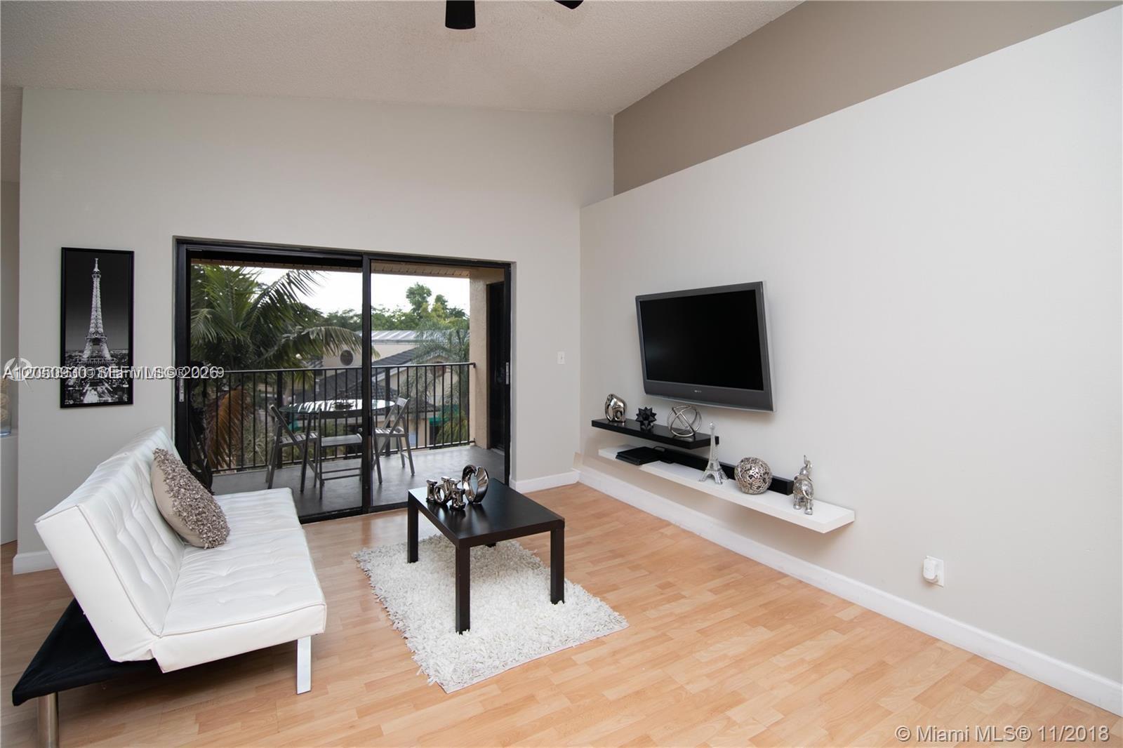 A living room features a white sofa, a black coffee table, and a wall-mounted television — 9999 Summerbreeze Dr # 403, Sunrise FL 33322, SUNRISE, FL