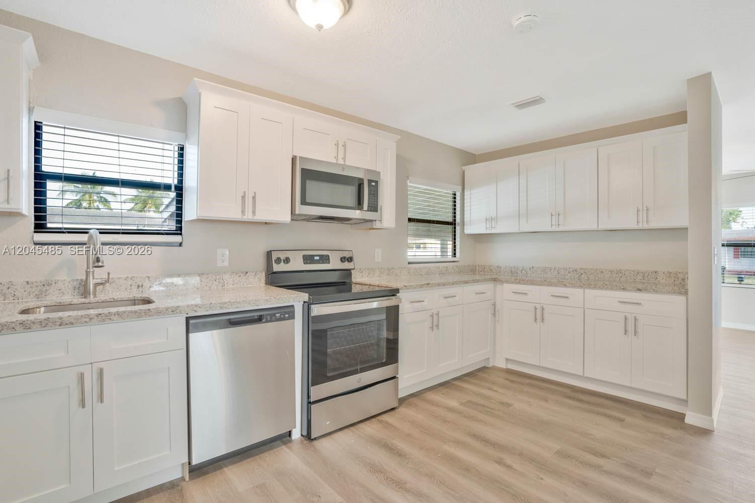A kitchen features white cabinets, stainless steel appliances, and light-colored granite countertops — FORT LAUDERDALE, FL