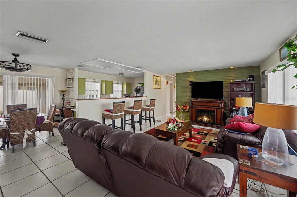 An open-concept living and dining area features a brick fireplace, tile floors, and kitchen bar — 12149 PARK BOULEVARD UNIT 7, SEMINOLE, FL
