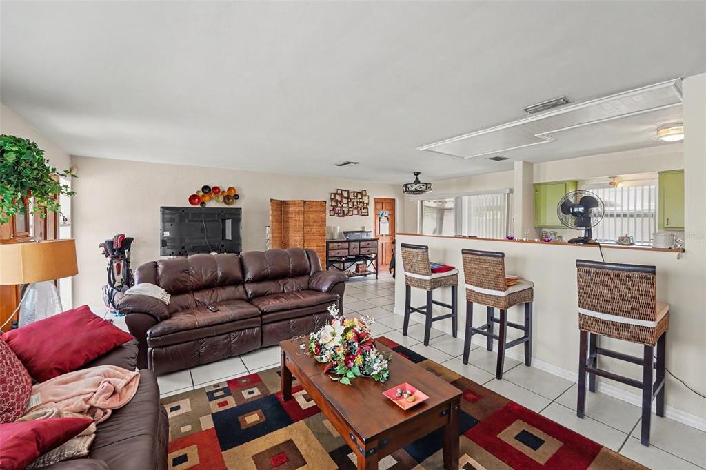A living room features a brown leather sofa, a patterned rug, and a kitchen breakfast bar — 12149 PARK BOULEVARD UNIT 7, SEMINOLE, FL
