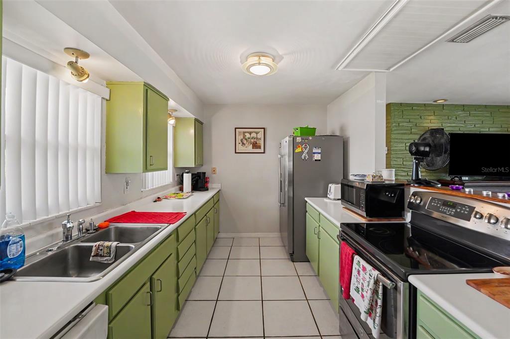 A kitchen features light green cabinets, white countertops, a stainless steel refrigerator, and tiled flooring — 12149 PARK BOULEVARD UNIT 7, SEMINOLE, FL