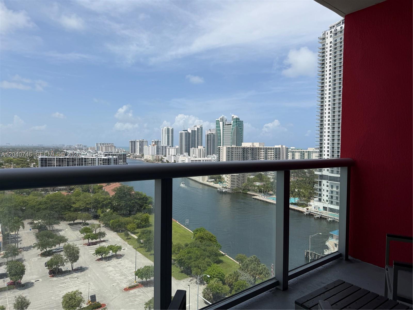 A balcony with a glass railing overlooks a waterway, parking lot, and city skyline — 2602 E Hallandale Beach Blvd # R1910, Hallandale Beach FL 33009, HALLANDALE BEACH, FL