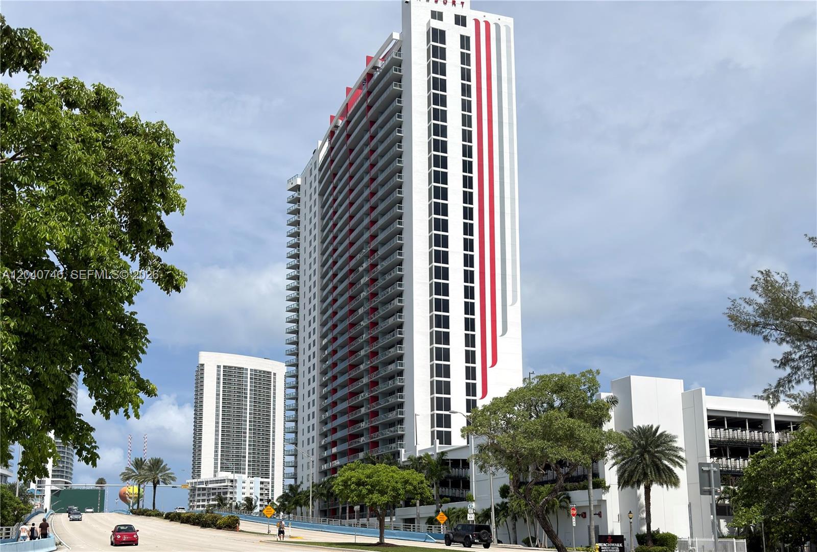 A tall, white high-rise building with red and grey vertical stripes stands near a road — 2602 E Hallandale Beach Blvd # R1910, Hallandale Beach FL 33009, HALLANDALE BEACH, FL