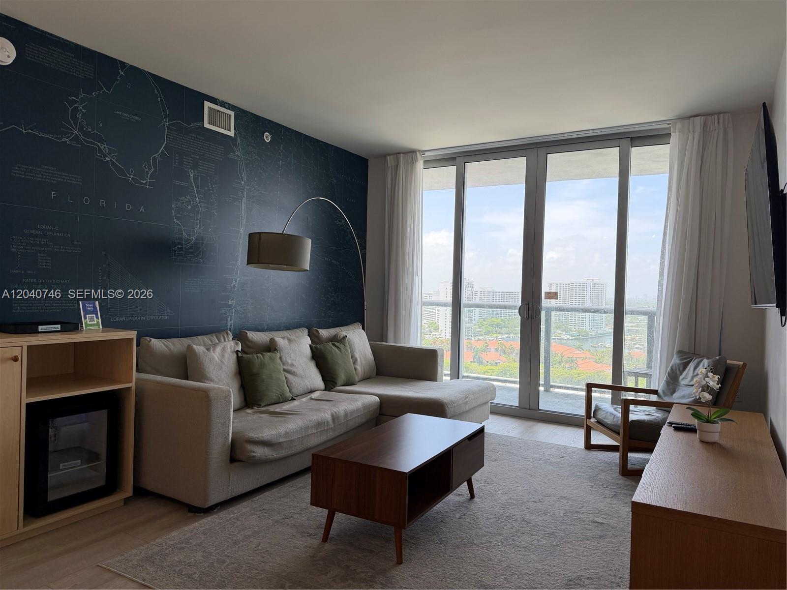 A living room features a sectional sofa, a map-patterned accent wall, and a balcony view — 2602 E Hallandale Beach Blvd # R1910, Hallandale Beach FL 33009, HALLANDALE BEACH, FL