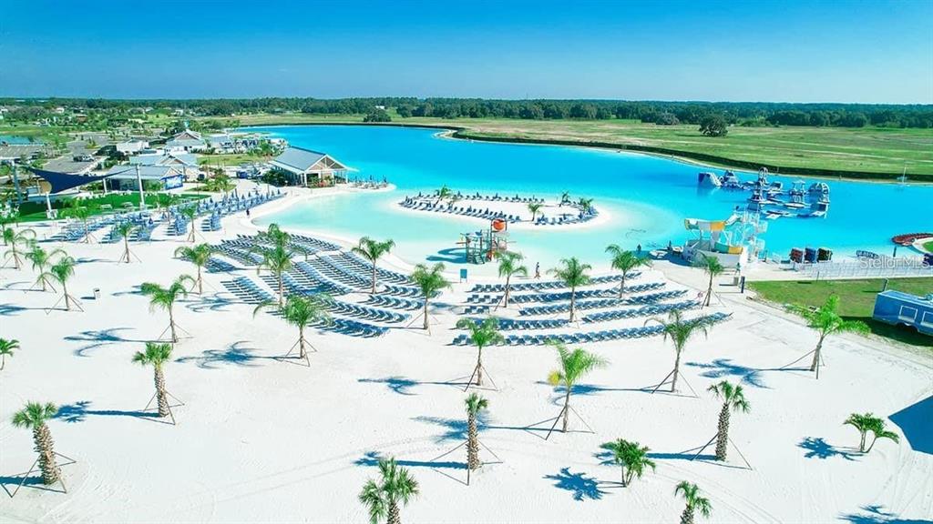An aerial view shows a large turquoise swimming lagoon with a sandy beach and palm trees — 32813 OSPREY PEAK WAY, SAN ANTONIO, FL
