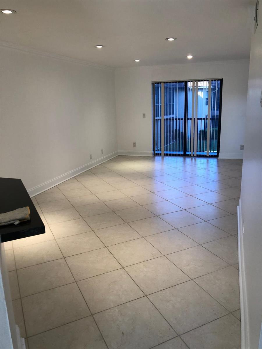 An empty living room with light-colored tile flooring, white walls, recessed lighting, and sliding glass doors — 21911 Lake Forest Circle # 204, Boca Raton FL 33433, BOCA RATON, FL