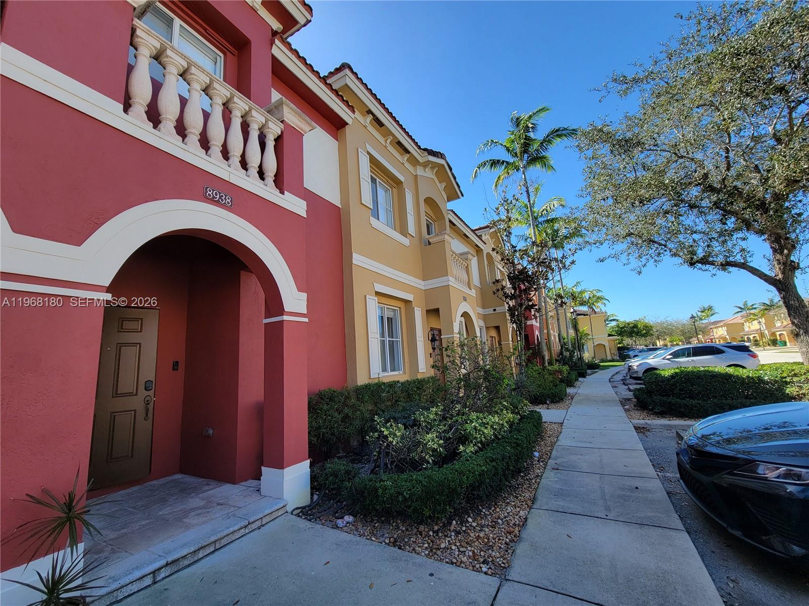 A red and tan multi-story townhouse exterior features a sidewalk, landscaping, and parked cars — 8938 SW 19th St # 904, Miramar FL 33025, MIRAMAR, FL