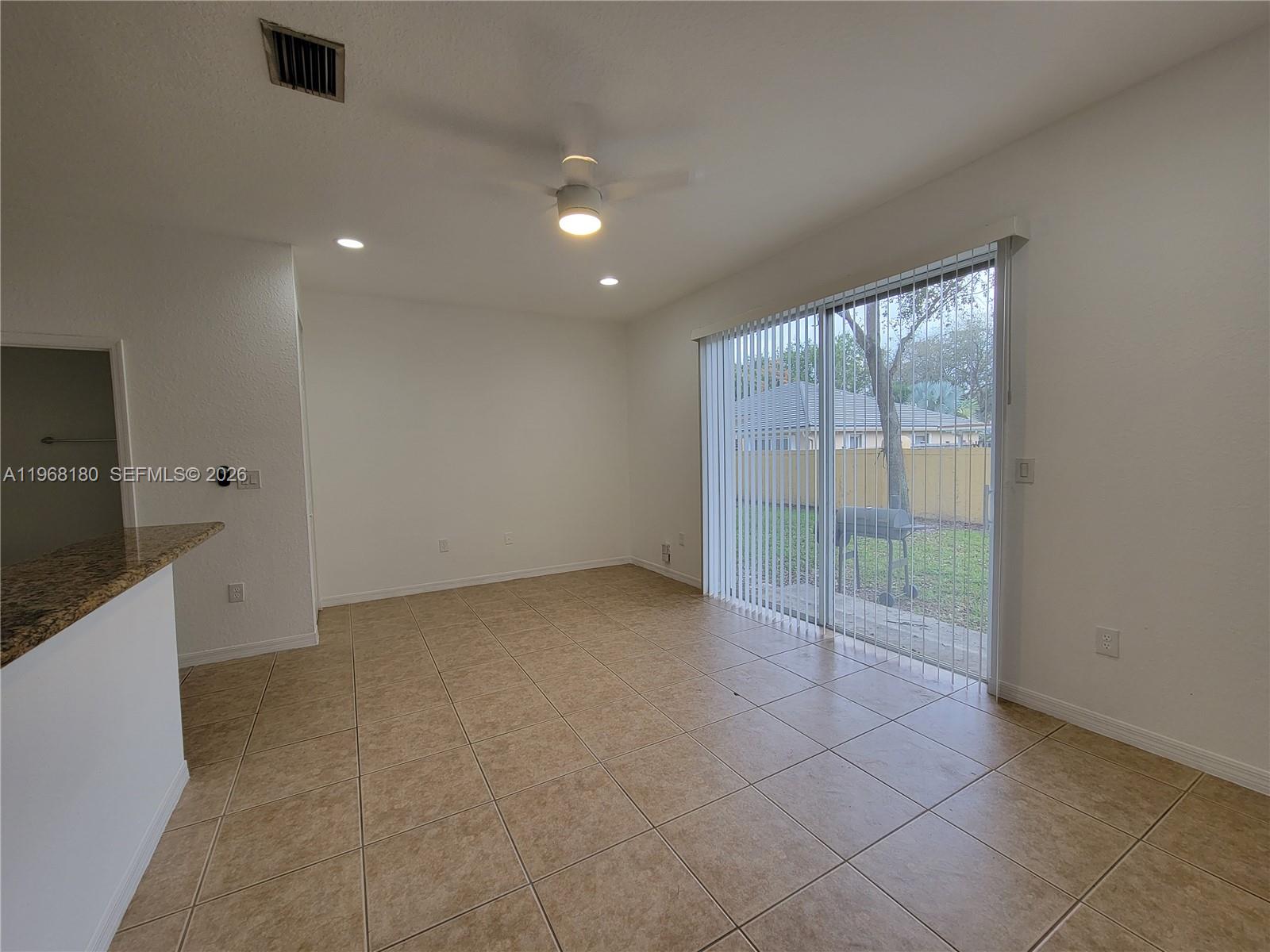 An empty room features beige tile flooring, a ceiling fan, and sliding glass patio doors — 8938 SW 19th St # 904, Miramar FL 33025, MIRAMAR, FL