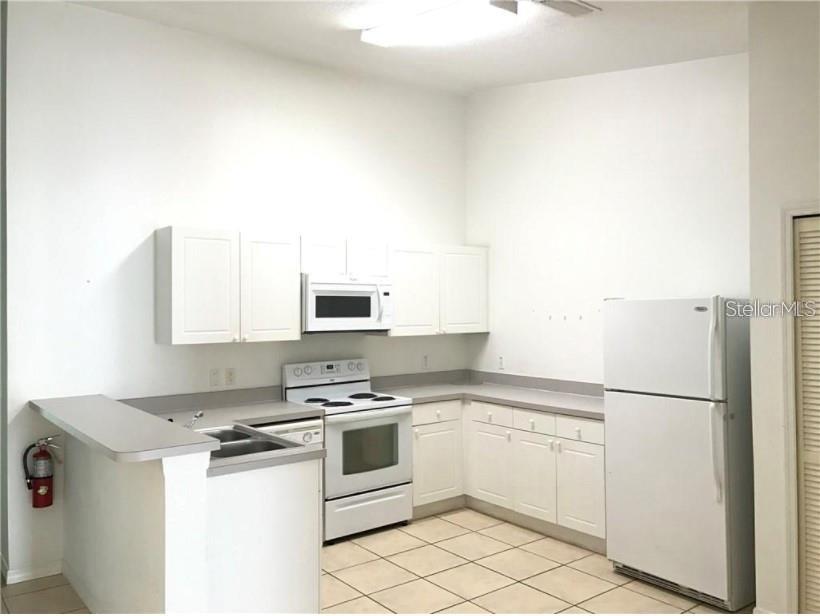 A kitchen features white cabinets, white appliances, a breakfast bar, and light-colored tile flooring — 2792 CLUB CORTILE CIRCLE UNIT B, KISSIMMEE, FL