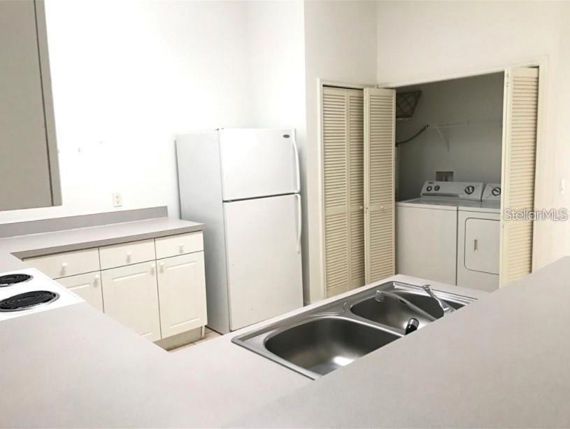 A kitchen features white cabinets, a refrigerator, a double sink, and an adjacent laundry closet — 2792 CLUB CORTILE CIRCLE UNIT B, KISSIMMEE, FL