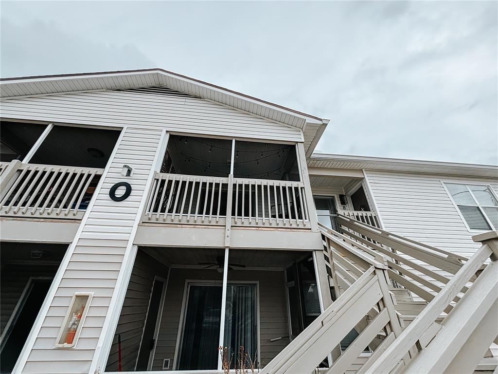 An exterior view of a two-story building with white siding, screened balconies, and wooden stairs — 1600 BIG TREE ROAD UNIT O8, DAYTONA BEACH, FL