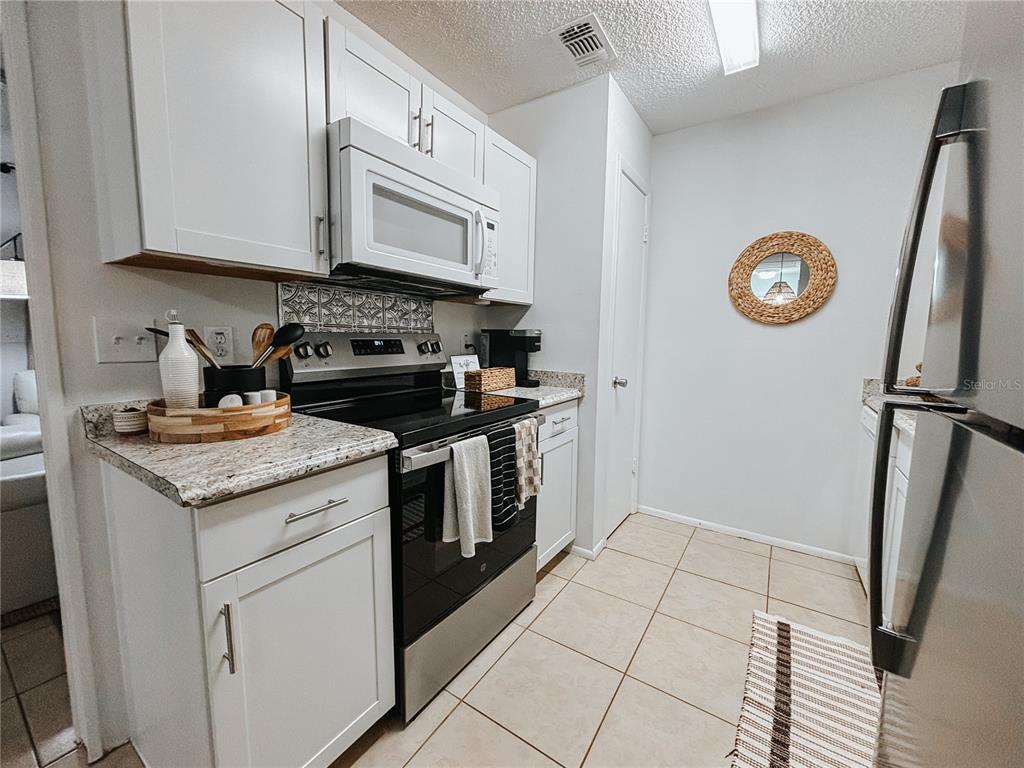 A galley kitchen features white cabinets, stainless steel appliances, and light-colored tile flooring — 1600 BIG TREE ROAD UNIT O8, DAYTONA BEACH, FL
