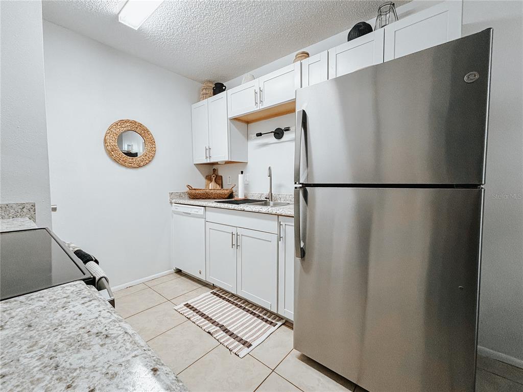 A kitchen features white cabinets, stainless steel appliances, granite countertops, and light tile flooring — 1600 BIG TREE ROAD UNIT O8, DAYTONA BEACH, FL