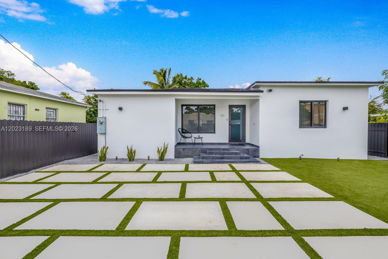 A white single-story house features a modern paved driveway, artificial turf, and a front porch — 121 NW 53rd St, Miami FL 33127, MIAMI, FL
