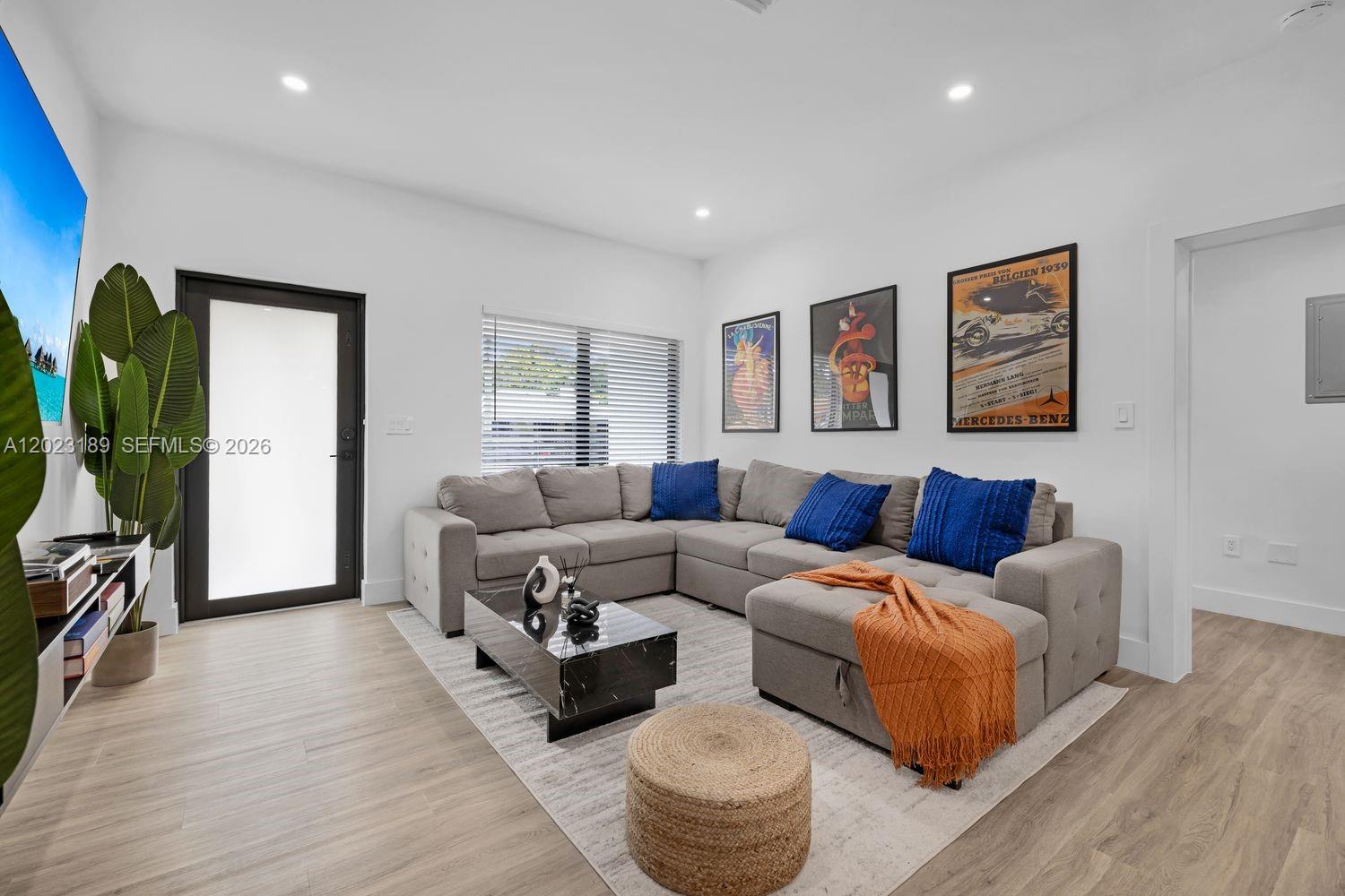 A living room features a grey sectional sofa, a coffee table, and three framed posters — 121 NW 53rd St, Miami FL 33127, MIAMI, FL