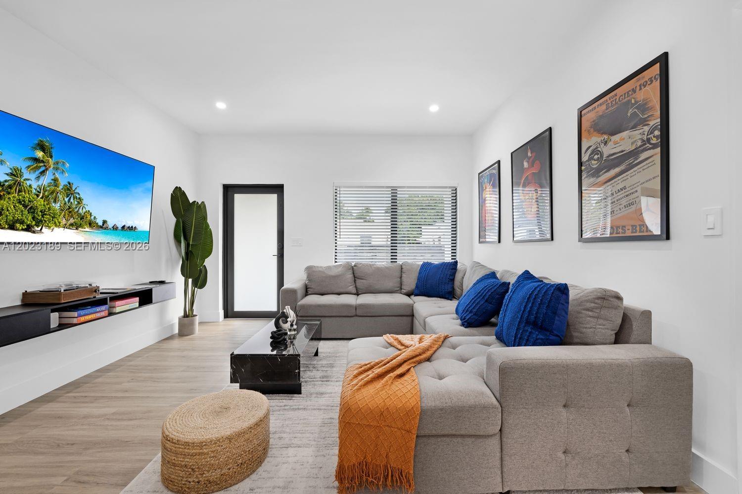 A modern living room features a gray sectional sofa, a wall-mounted television, and framed posters — 121 NW 53rd St, Miami FL 33127, MIAMI, FL
