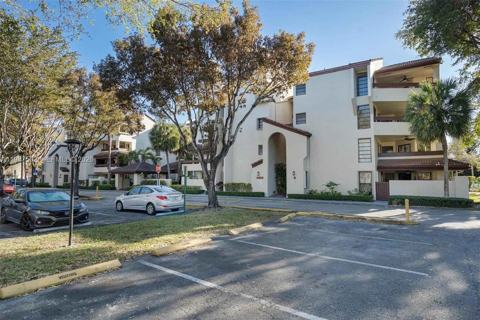 A multi-story apartment building exterior with a parking lot and trees in the foreground — 9040 SW 125th Ave # D408, Miami FL 33186, MIAMI, FL