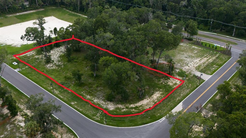 An aerial view shows a vacant, tree-covered corner lot outlined in red between two roads — 1704 MAGNOLIA BLUFF CIR, DELAND, FL