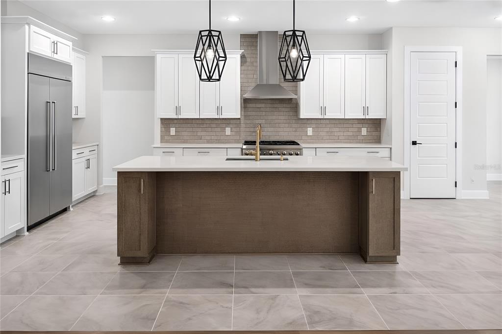 A modern kitchen features white cabinets, a brown island, stainless steel appliances, and tile flooring — 1704 MAGNOLIA BLUFF CIR, DELAND, FL