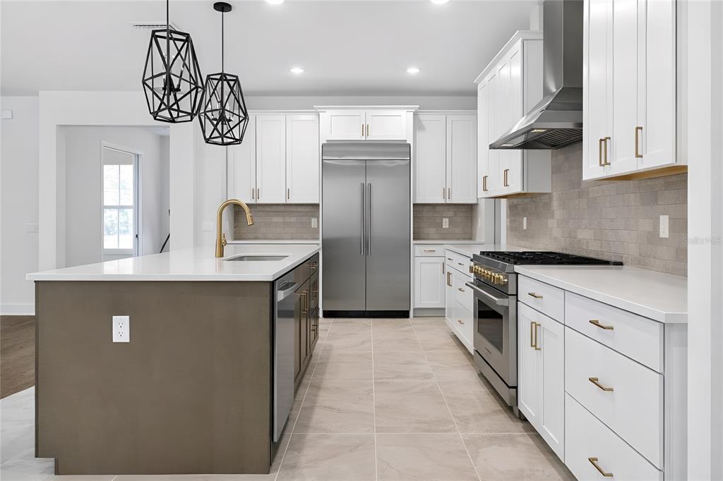 A modern kitchen features white cabinets, a dark island, stainless steel appliances, and tile flooring — 1704 MAGNOLIA BLUFF CIR, DELAND, FL