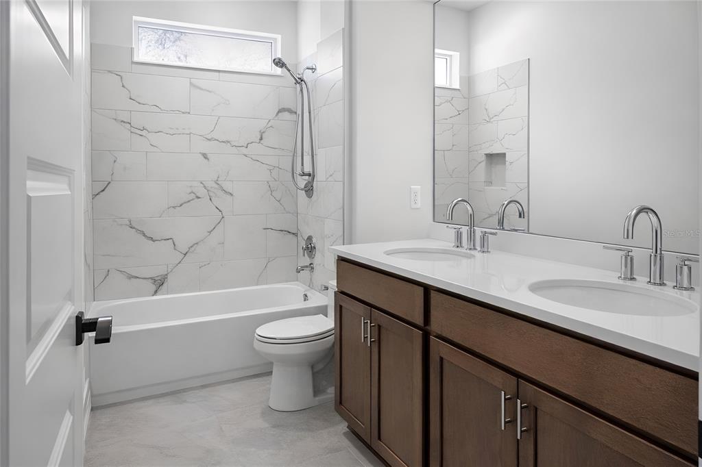A bathroom with a double vanity, wood cabinets, and a tub-shower combo with marble tile — 1704 MAGNOLIA BLUFF CIR, DELAND, FL