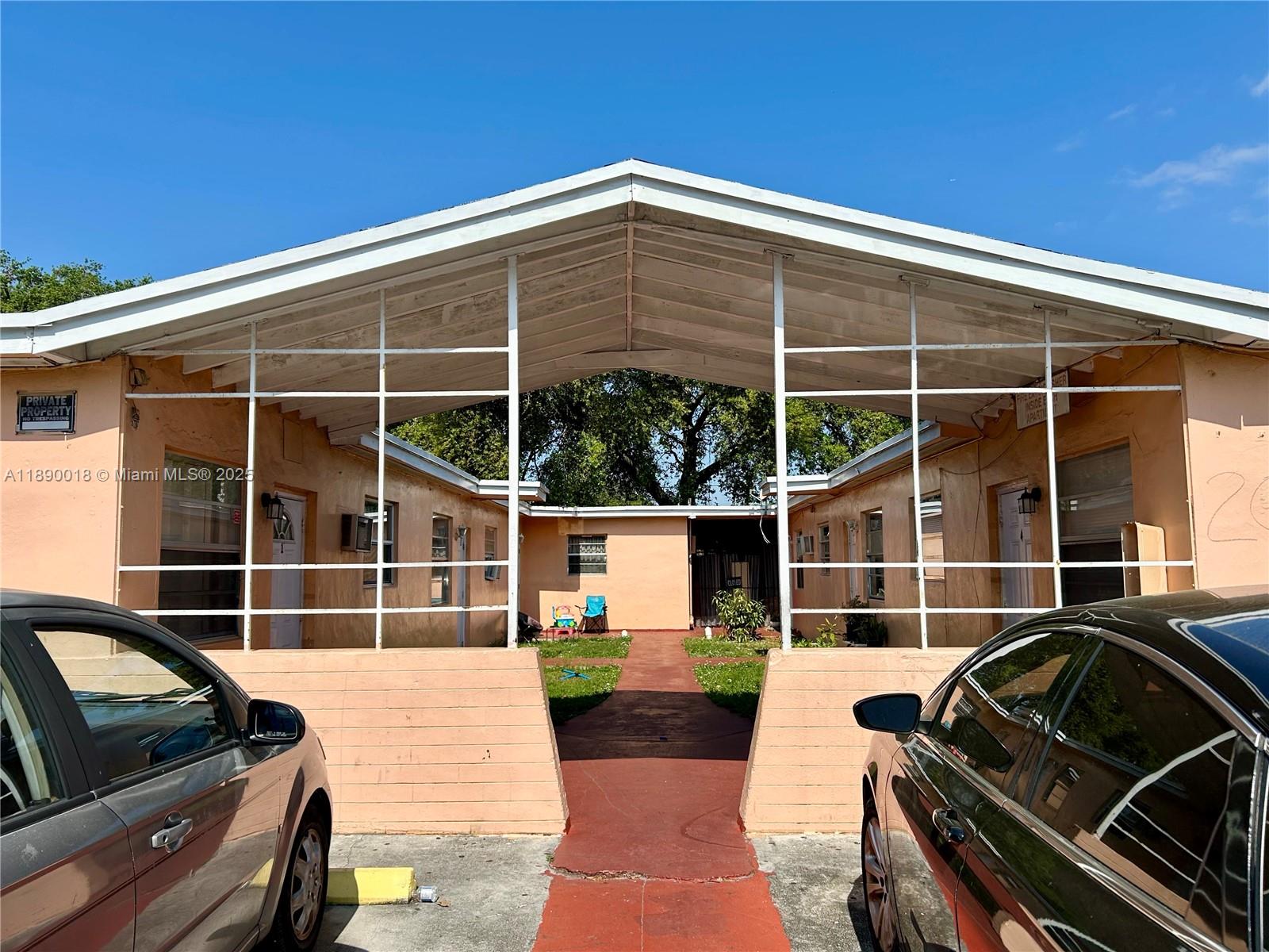 An exterior view of a peach-colored apartment complex with a central walkway and carport — 2013 Washington Ave, Opa-Locka FL 33054, OPA-LOCKA, FL