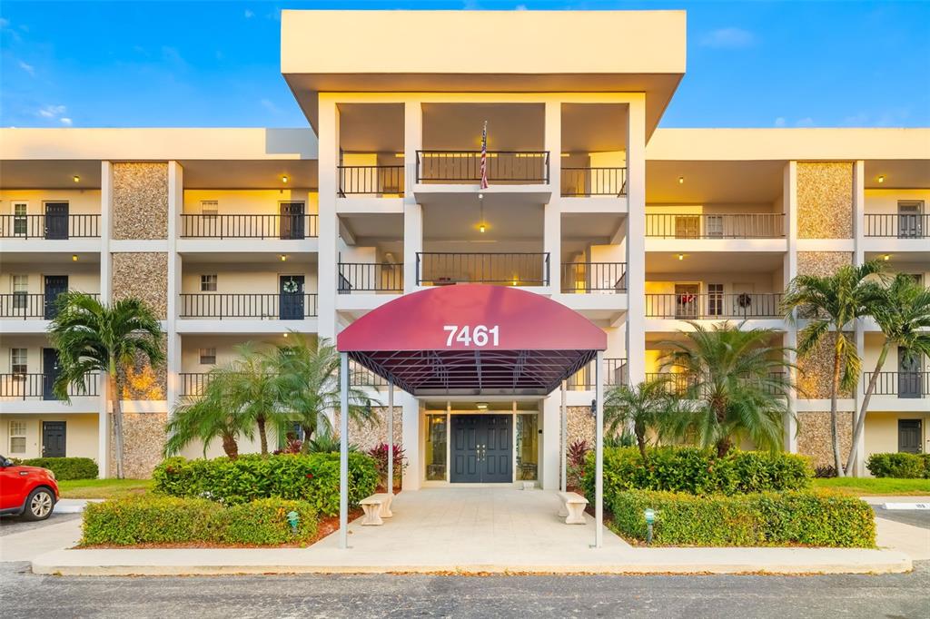 A multi-story apartment building features a central entrance with a red awning and palm trees — 7461 W COUNTRY CLUB DRIVE UNIT 404, SARASOTA, FL