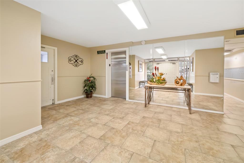 A tiled lobby features a metal elevator, a mirrored wall, and a decorative console table — 7461 W COUNTRY CLUB DRIVE UNIT 404, SARASOTA, FL