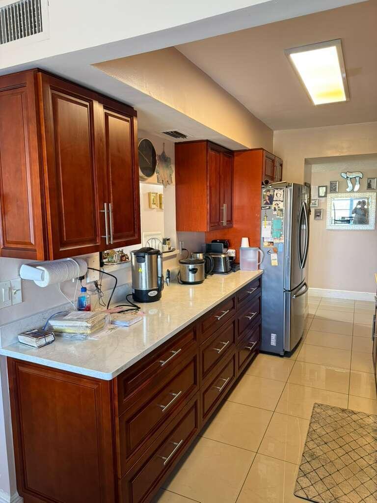 A kitchen with cherry wood cabinets, white countertops, stainless steel appliances, and beige tile flooring — 4164 Inverrary Drive # 302, Lauderhill FL 33319, LAUDERHILL, FL