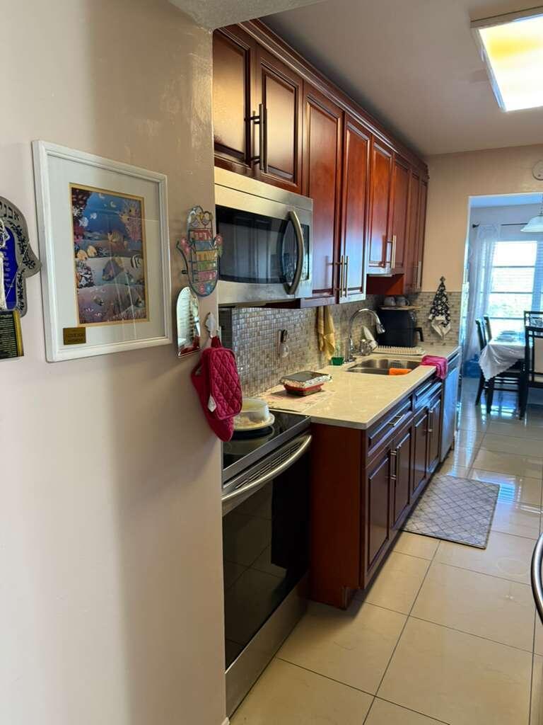 A galley-style kitchen features dark wood cabinets, stainless steel appliances, and light-colored countertops — 4164 Inverrary Drive # 302, Lauderhill FL 33319, LAUDERHILL, FL
