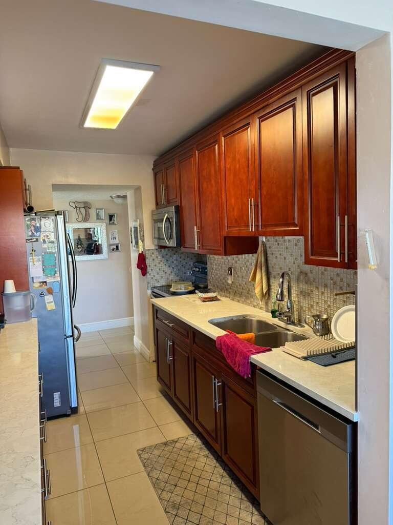 A galley kitchen features cherry wood cabinets, stainless steel appliances, and light-colored tile flooring — 4164 Inverrary Drive # 302, Lauderhill FL 33319, LAUDERHILL, FL