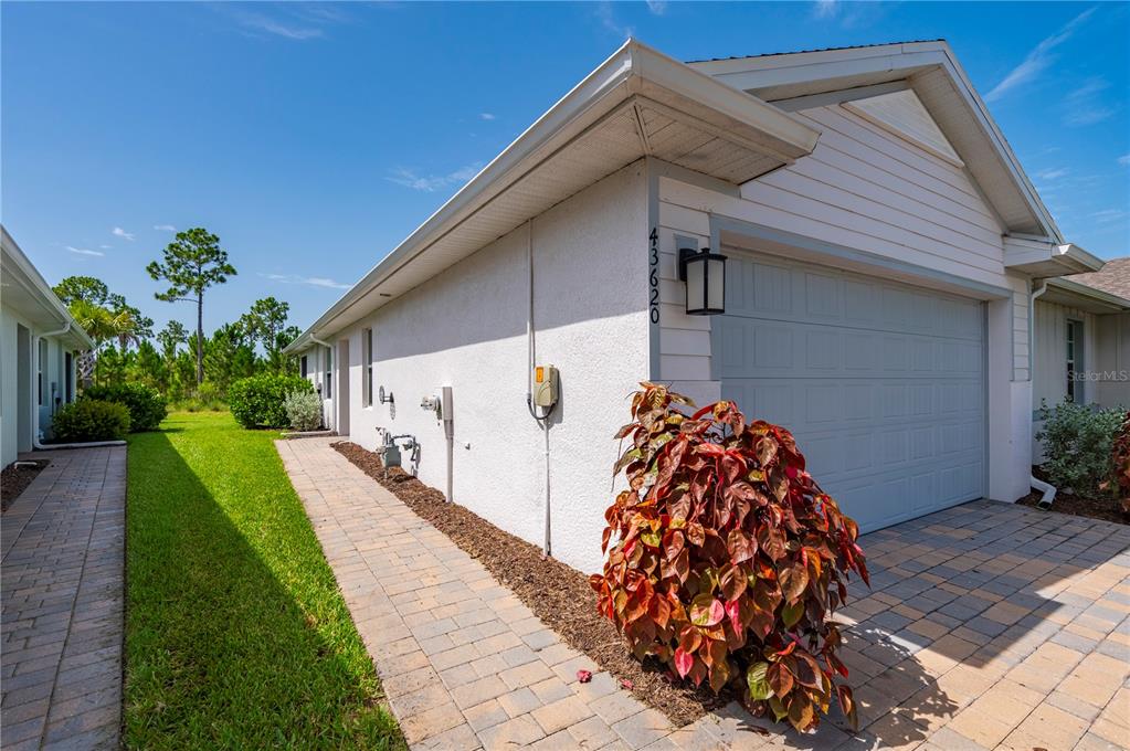 A side view of a house exterior featuring a garage, a paved walkway, and landscaping — 43620 SPARROW DRIVE, PUNTA GORDA, FL