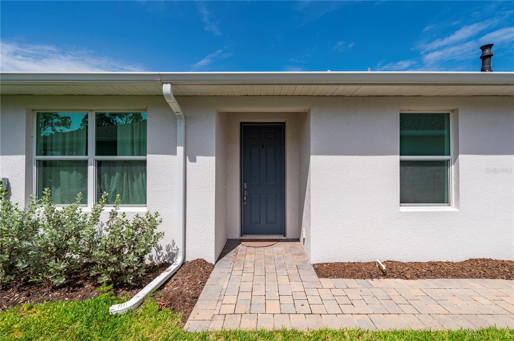 A white stucco house exterior features a dark gray front door and a paver walkway — 43620 SPARROW DRIVE, PUNTA GORDA, FL