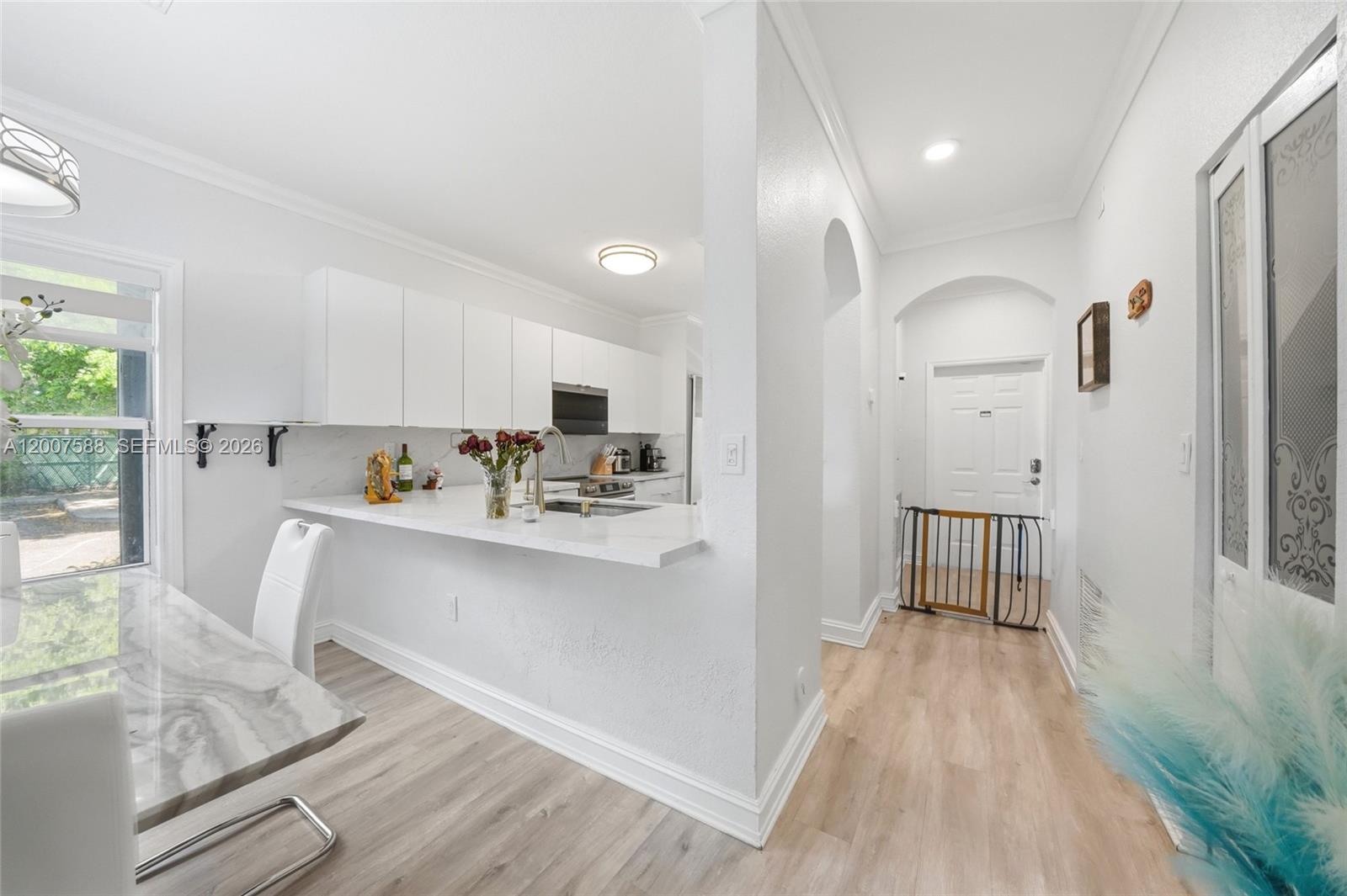 A kitchen with white cabinets and a breakfast bar opens to a hallway with flooring — MIRAMAR, FL