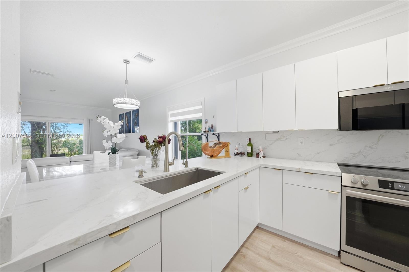 A modern kitchen features white cabinets, marble countertops, stainless steel appliances, and a farmhouse sink — MIRAMAR, FL